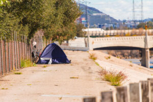 a tent and makeshift shelter beside a river, representing homelessness in America